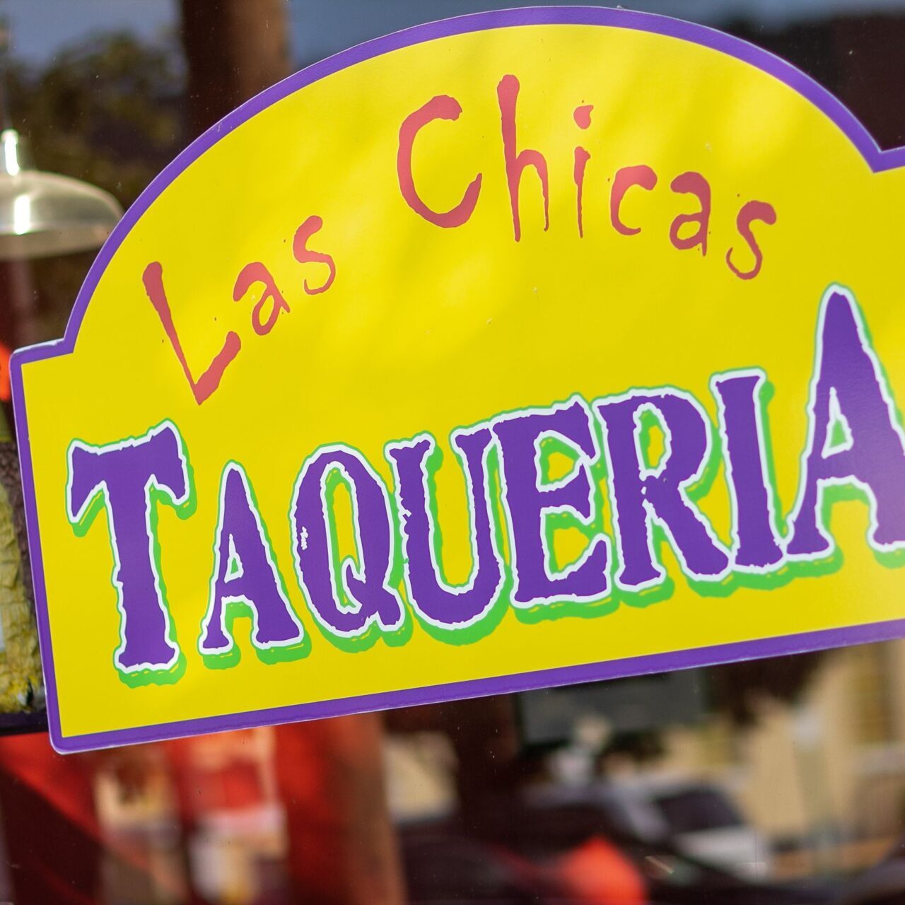 Bright yellow sign with "Las Chicas Taqueria" written in colorful letters