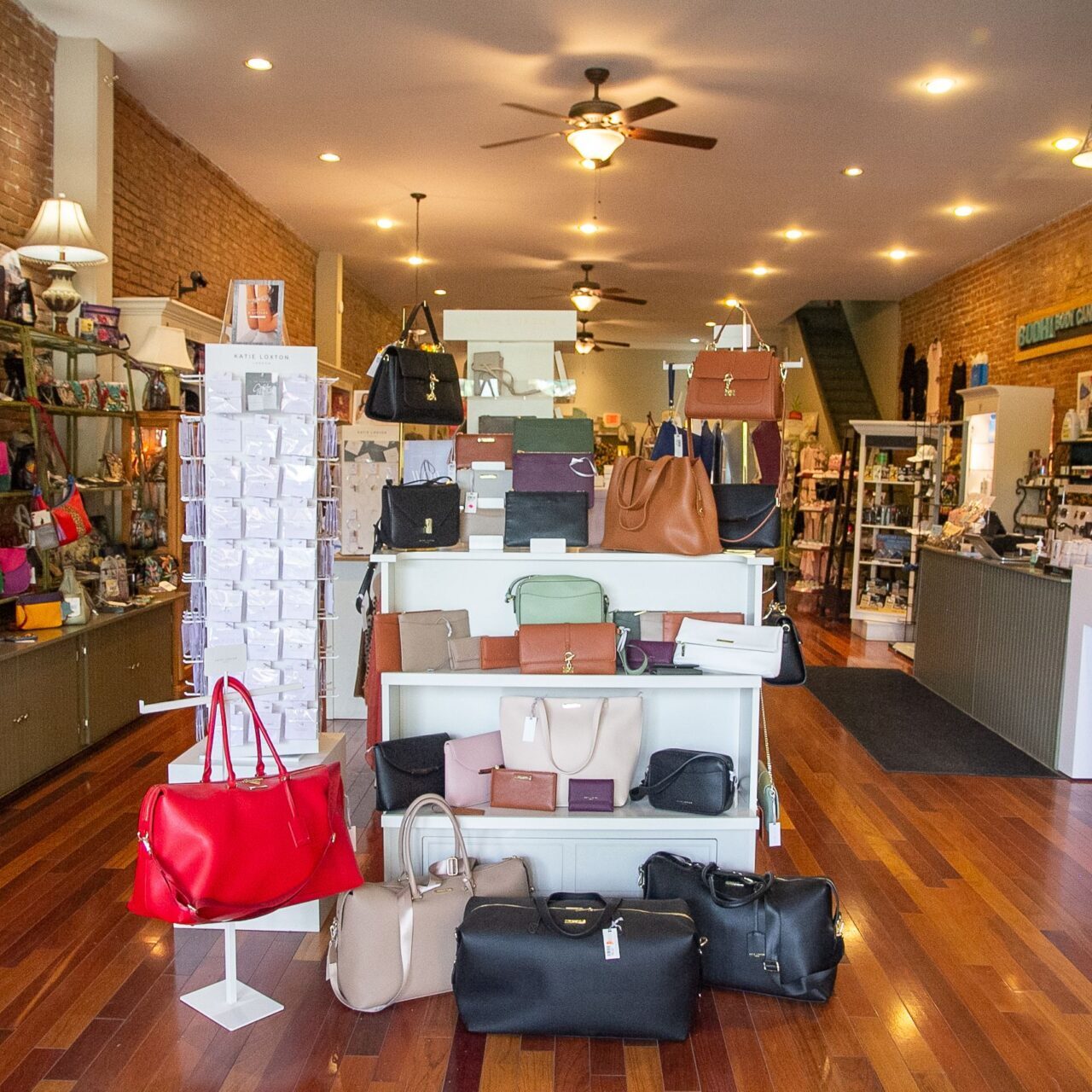 inside of store with brick walls, dark hardwood floors, and a wide variety of purses for sale